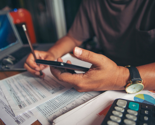 Side view of man holding mobile phone and pen while filling out financial documents