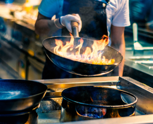 Chef in restaurant kitchen at stove with pan, cooking food